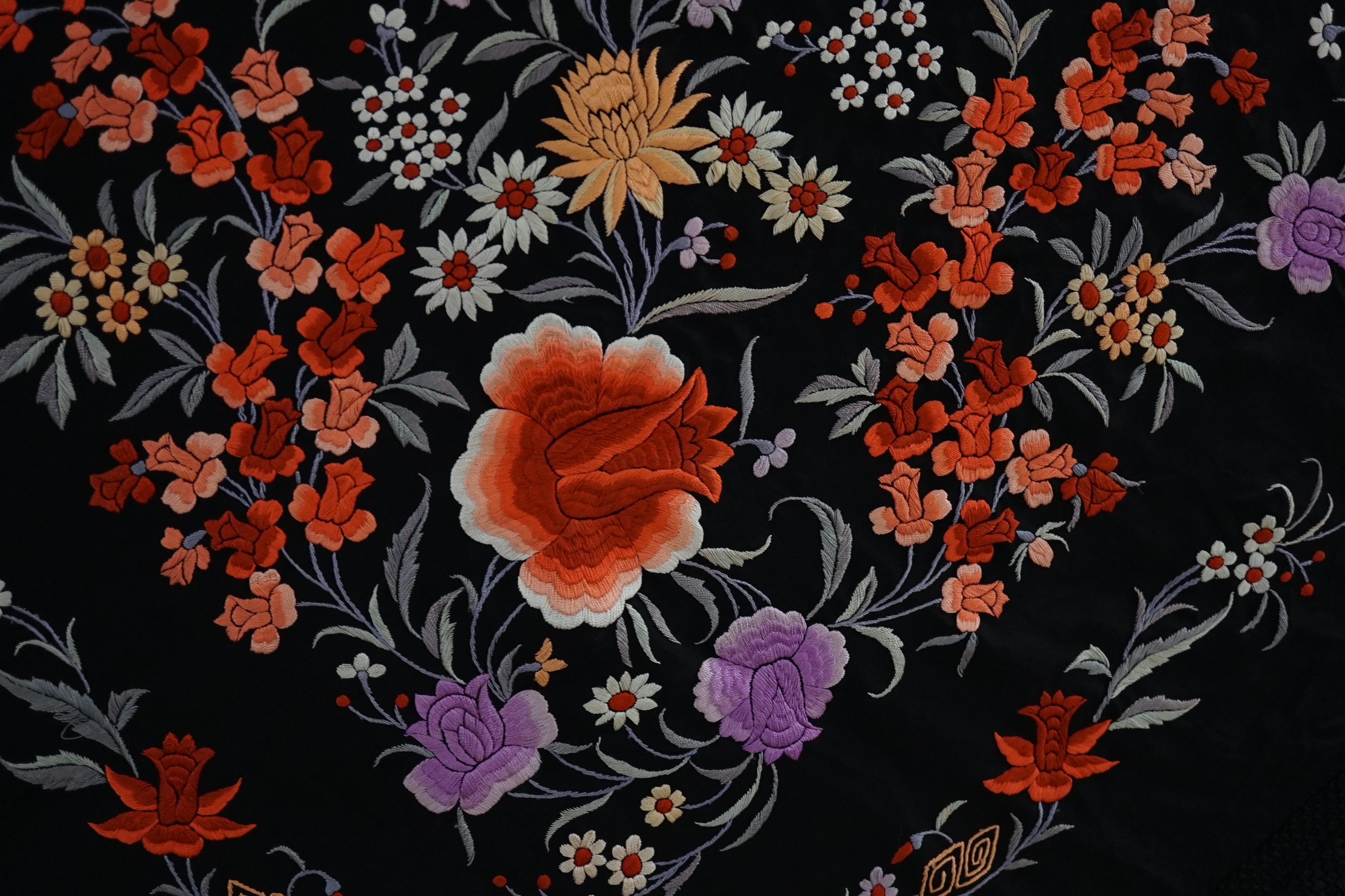 A late 19th / early 20th century Chinese black silk shawl, with polychrome silk embroidered flowers in green, red, orange, lilac, yellow and white, the centre embroidered with, sprigs of multi-coloured flowers, the four